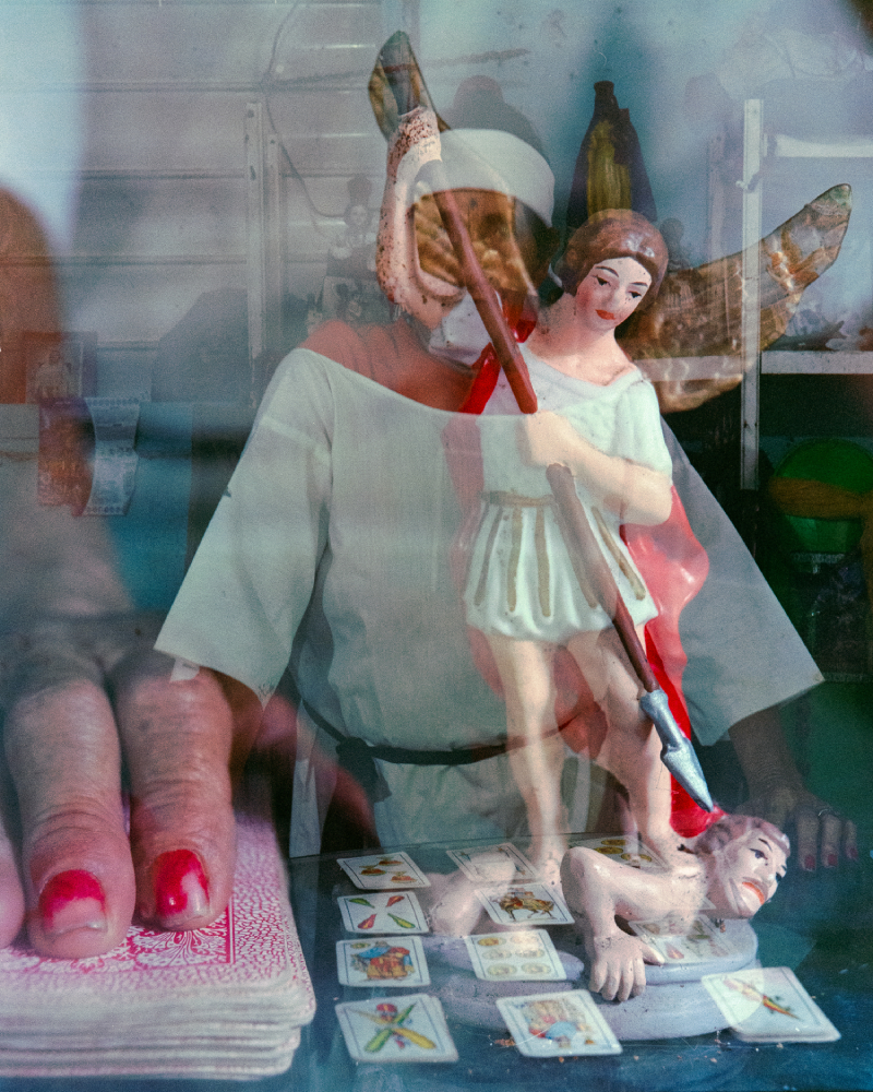 An angel holding a spear to a man's head, superimposed over a close up of a hand and cards