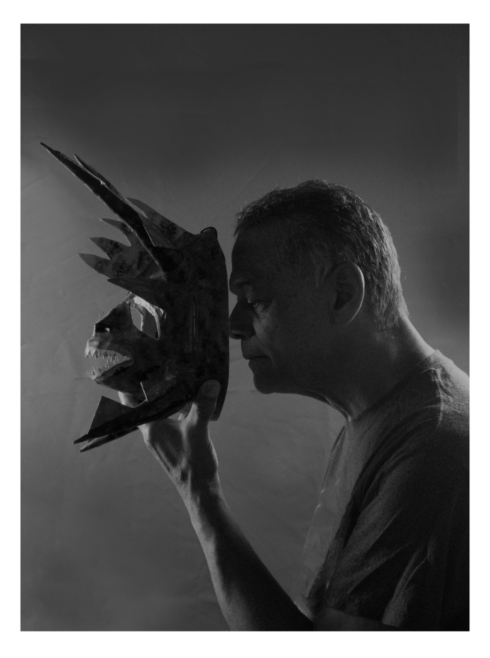 Portrait of a man in profile holding a mask in front of his face