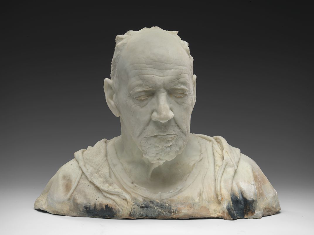 A cast sculpture bust of a balding old man with eyes closed.