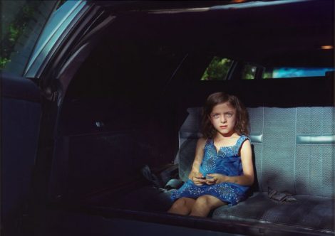 Small girl stares accusingly from the darkness of the backseat of a car.