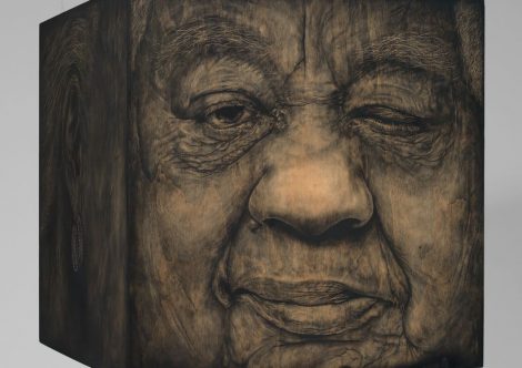 A large wooden cube, with an elderly face drawn on it in charcoal.